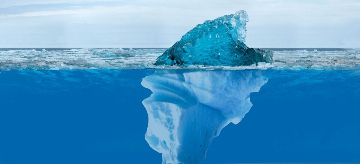 Bild på ett isberg som står i blått hav, där man ser en mindre del ovan vattnet och man anar resten under vattenytan.