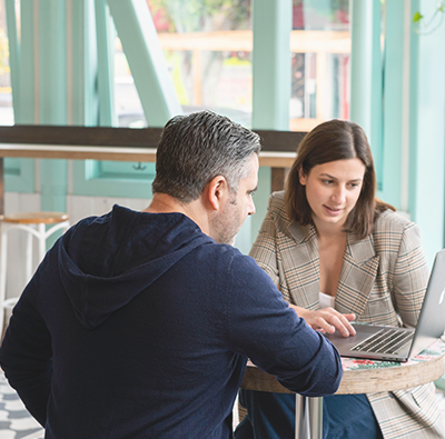 En man och en kvinna sitter vid ett mindre bord i ett café el liknande och tittar på en laptop.