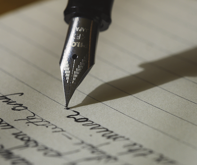 Detalj på en gammaldags bläckpenna som skriver på ett linjerat papper.