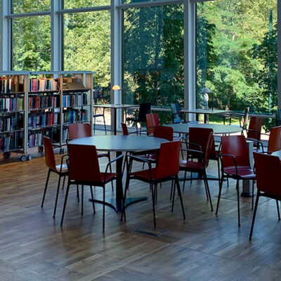 Interiörbild från en lokal med runda bord, stolar och hyllor vid stora glaspartier mot grönskande natur. För att illustrera hyresupphandlingar.