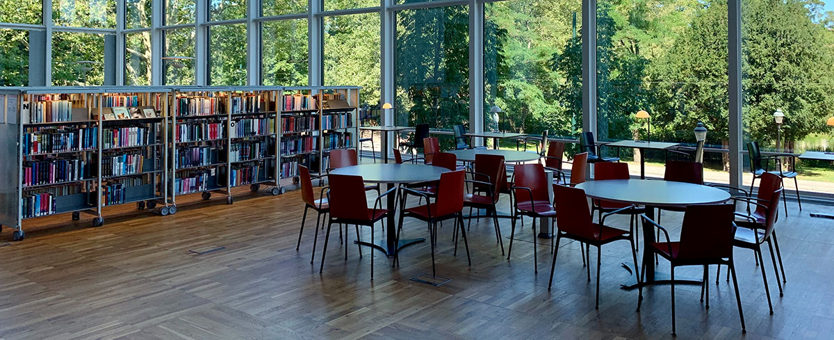 Interiörbild från en lokal med runda bord, stolar och hyllor vid stora glaspartier mot grönskande natur. För att illustrera hyresupphandlingar.