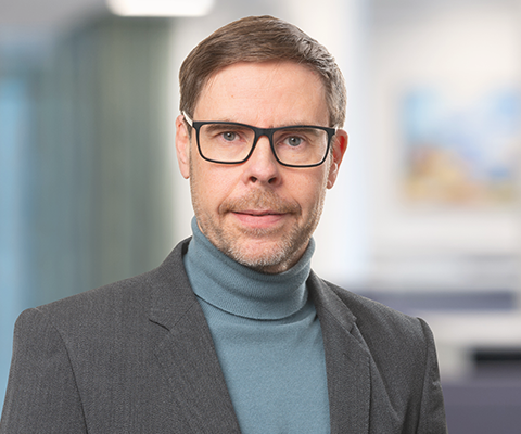 Inomhusporträtt på en man i blå polotröja, kavaj och glasögon.