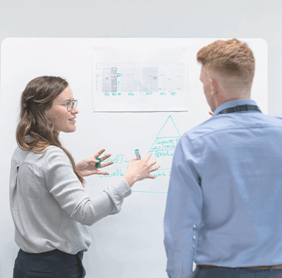 Man ser ryggarna på en kvinna och en man som står framför en white board med data på.