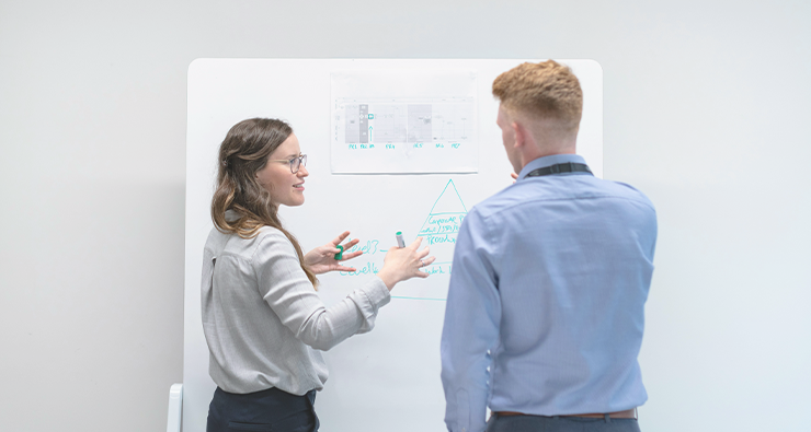 Man ser ryggarna på en kvinna och en man som står framför en white board med data på.