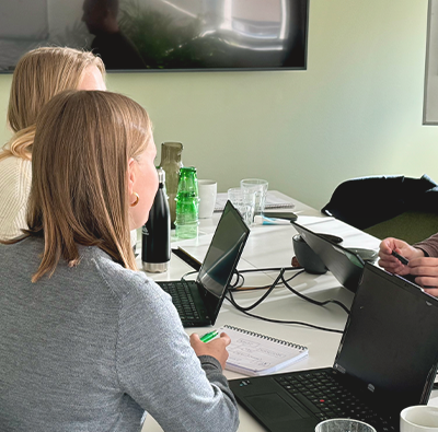 En man och två kvinnor sitter och arbetar vid ett bord i ett grönt konferensrum.